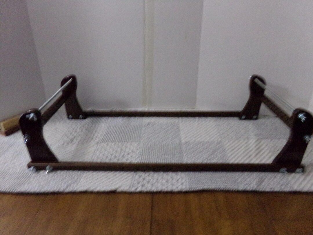 A dark wood Gerdan-style loom lying flat with the stand folded
