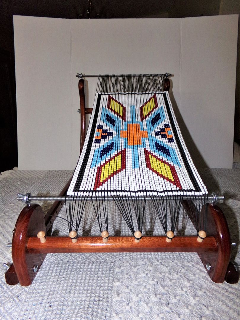 A dark wood Gerdan-style Foxfire loom on its stand, holding a finished panel of beadwork in a bold star design